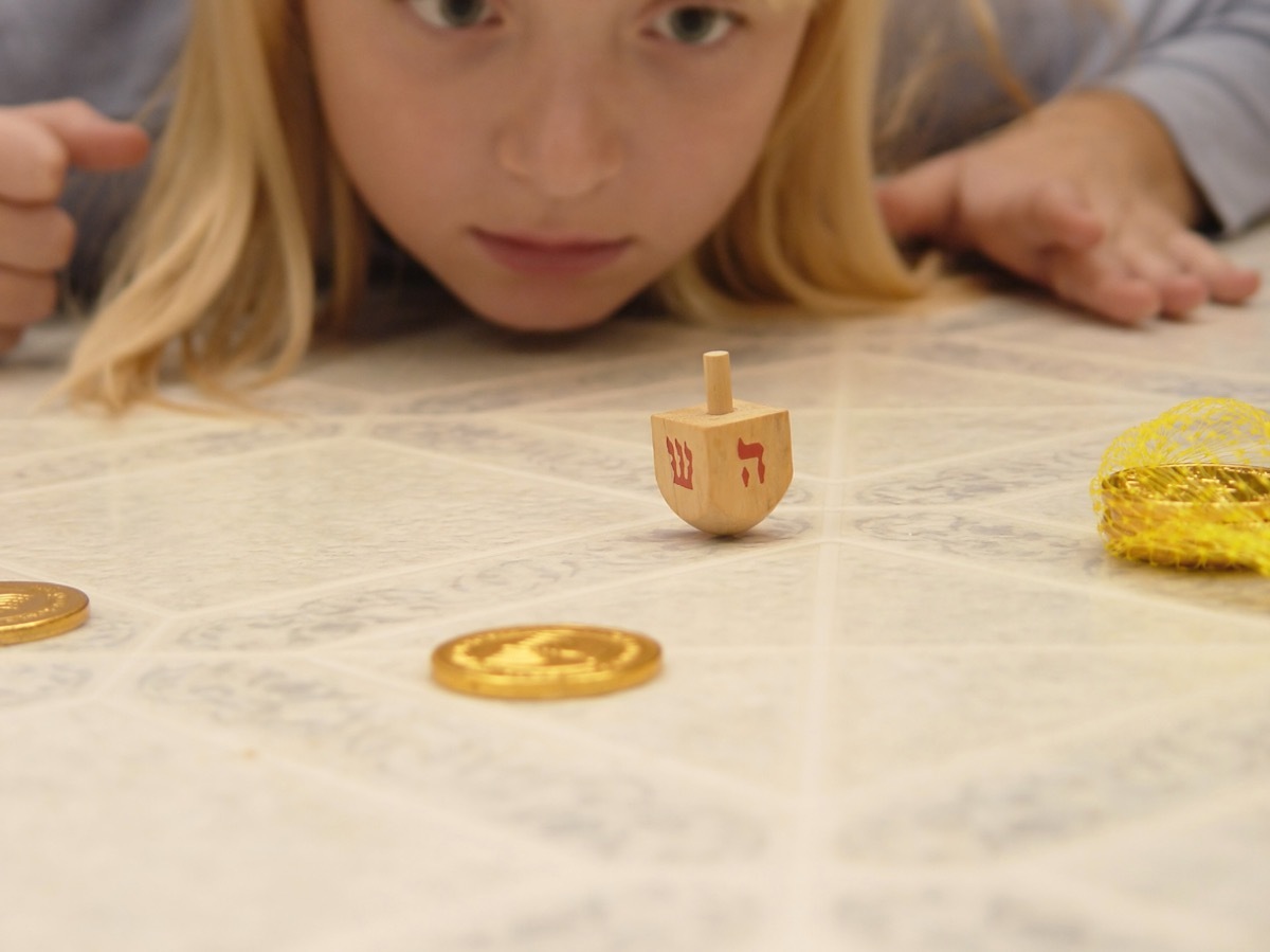 young blonde girl playing dreidel with gelt on table