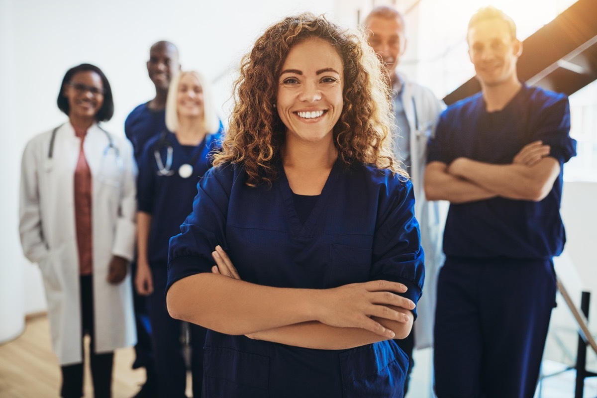 Young female doctor smiling while standing in a hospital corridor with a diverse group of staff in the background