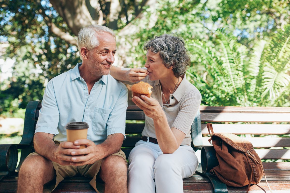 A senior couple sitting on a bench while eating a snack and drinking coffee