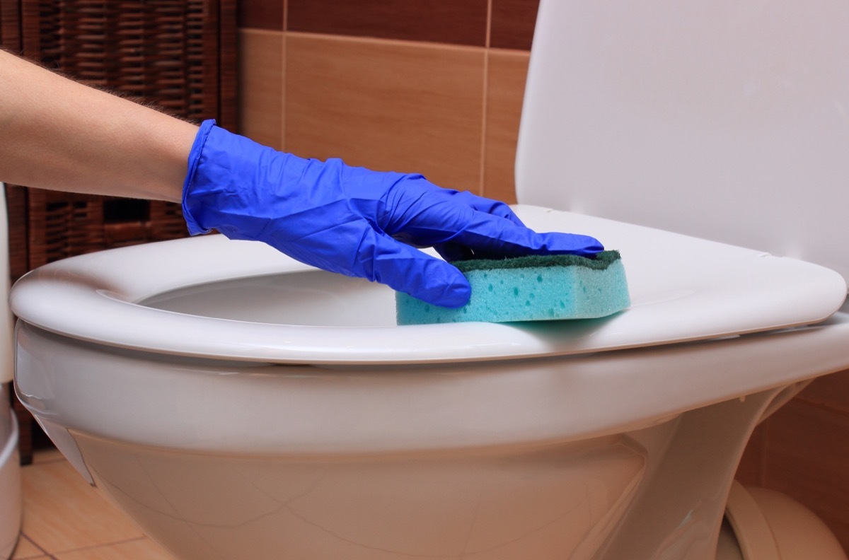 gloved hand cleaning toilet with sponge