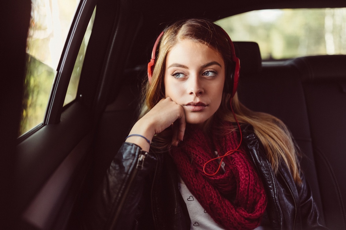 white teenage girl bored in the backseat with headphones on a road trip