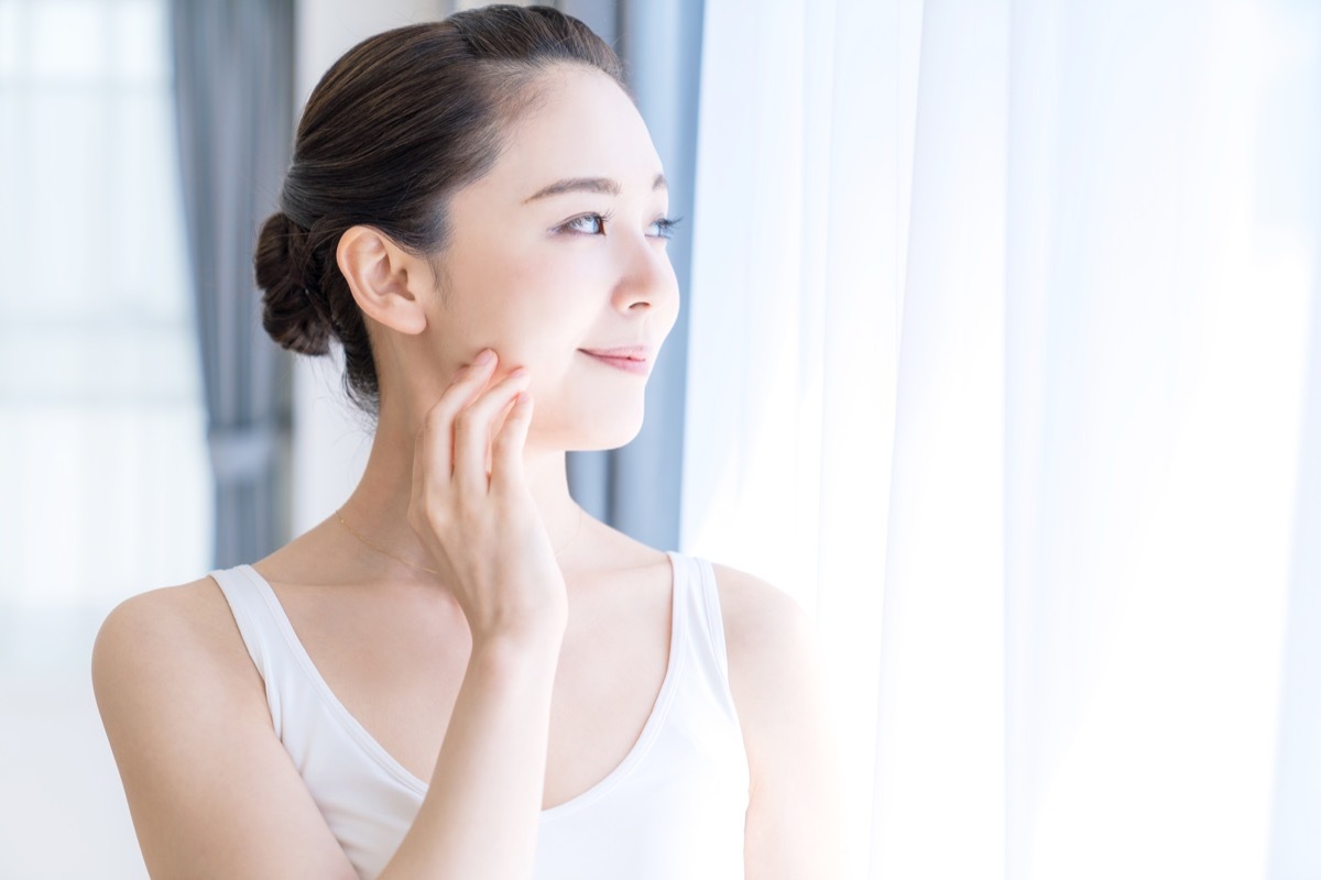 woman touching her face while staring out the window