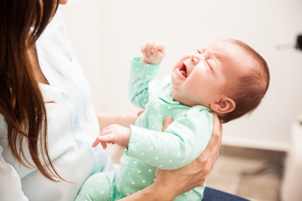 woman holding crying baby in green onesie