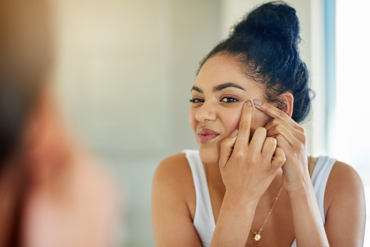 Woman touching at a pimple on her face in the mirror.