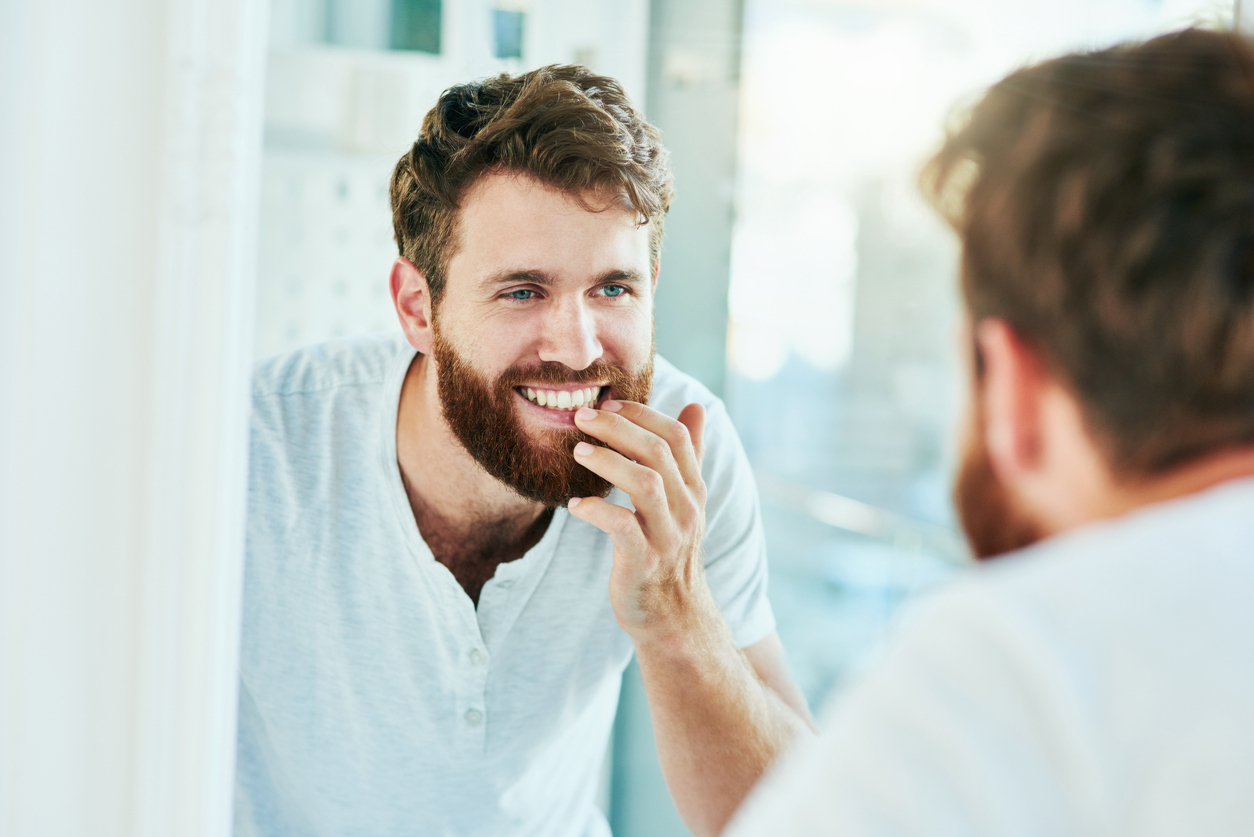 A young man smiling while looking at this teeth in the mirror