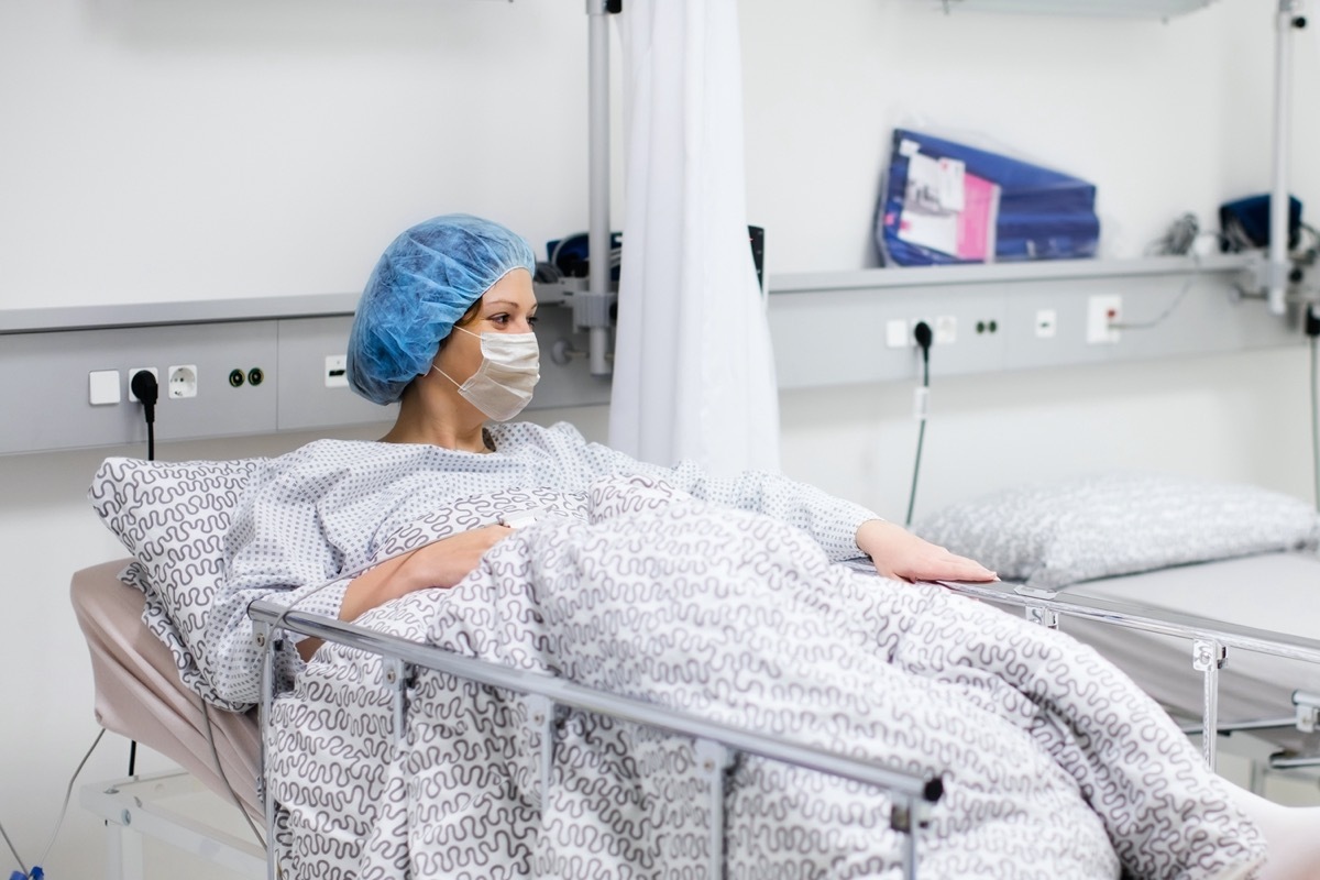 Young woman wearing face mask in clinic ward recovering from coronavirus disease. Sick