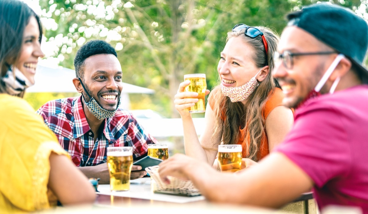 Friends drinking beer with opened face masks - New normal lifestyle concept with people having fun together talking on happy hour at brewery bar - Bright vivid filter with focus on afroamerican guy