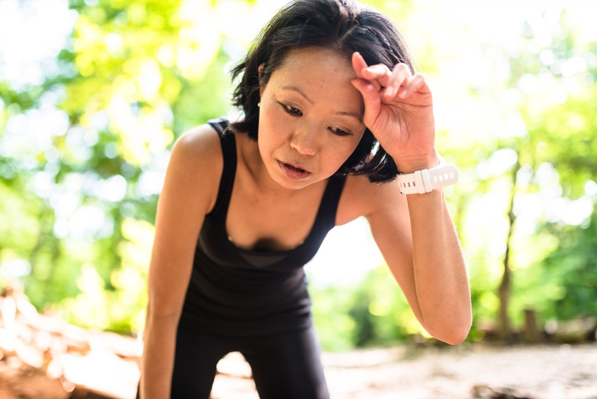 tired asian woman wiping her brow on an outdoor hike