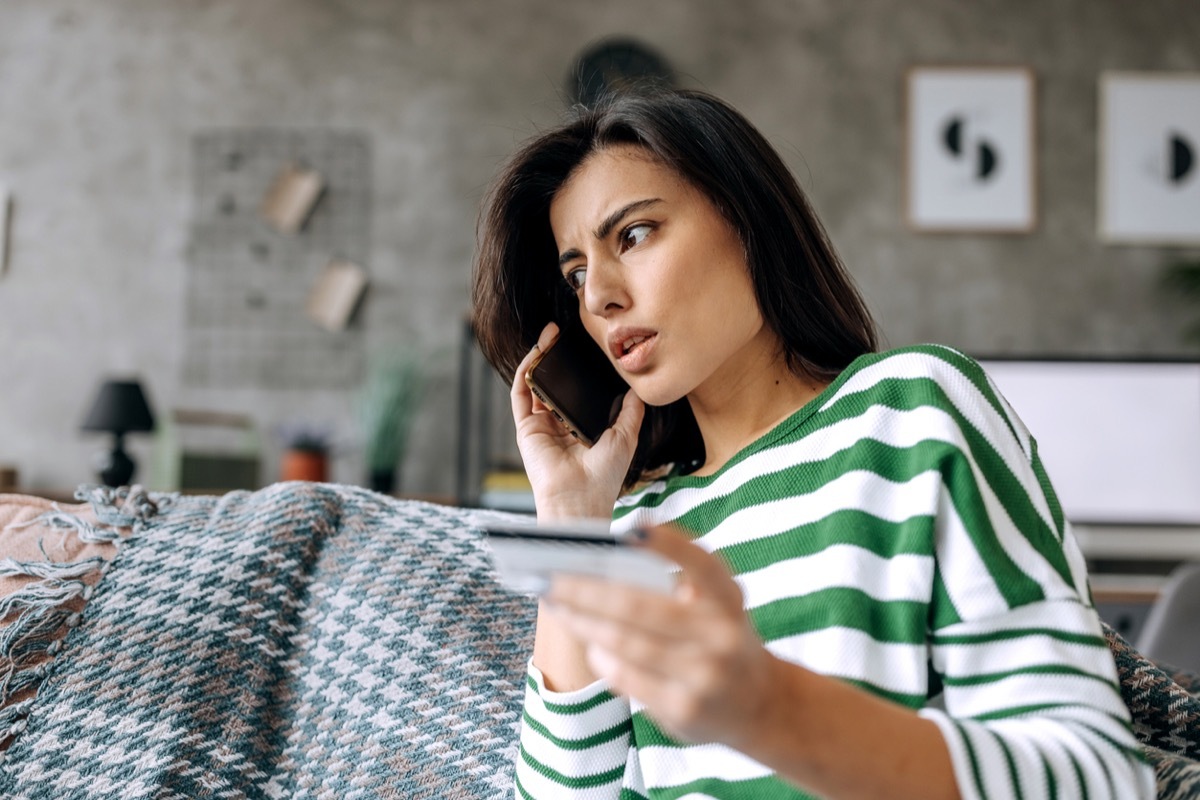 upset young woman talking on her cell phone while holding a credit card in her hand