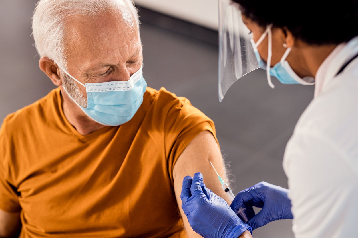 A senior man wearing a face mask receives a COVID-19 vaccine from a health care worker