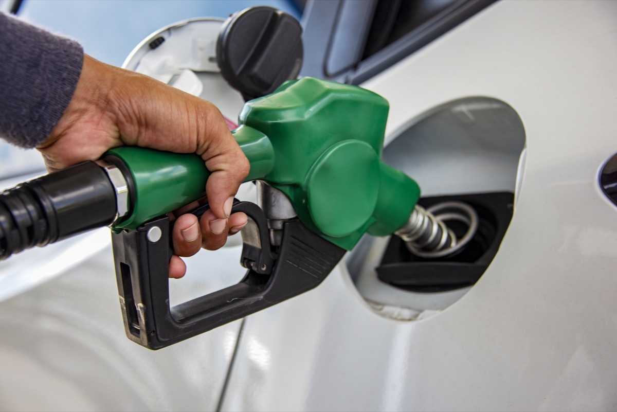 Man Handle pumping gasoline fuel nozzle to refuel. Vehicle fueling facility at petrol station. White car at gas station being filled with fuel. Transportation and ownership concept.