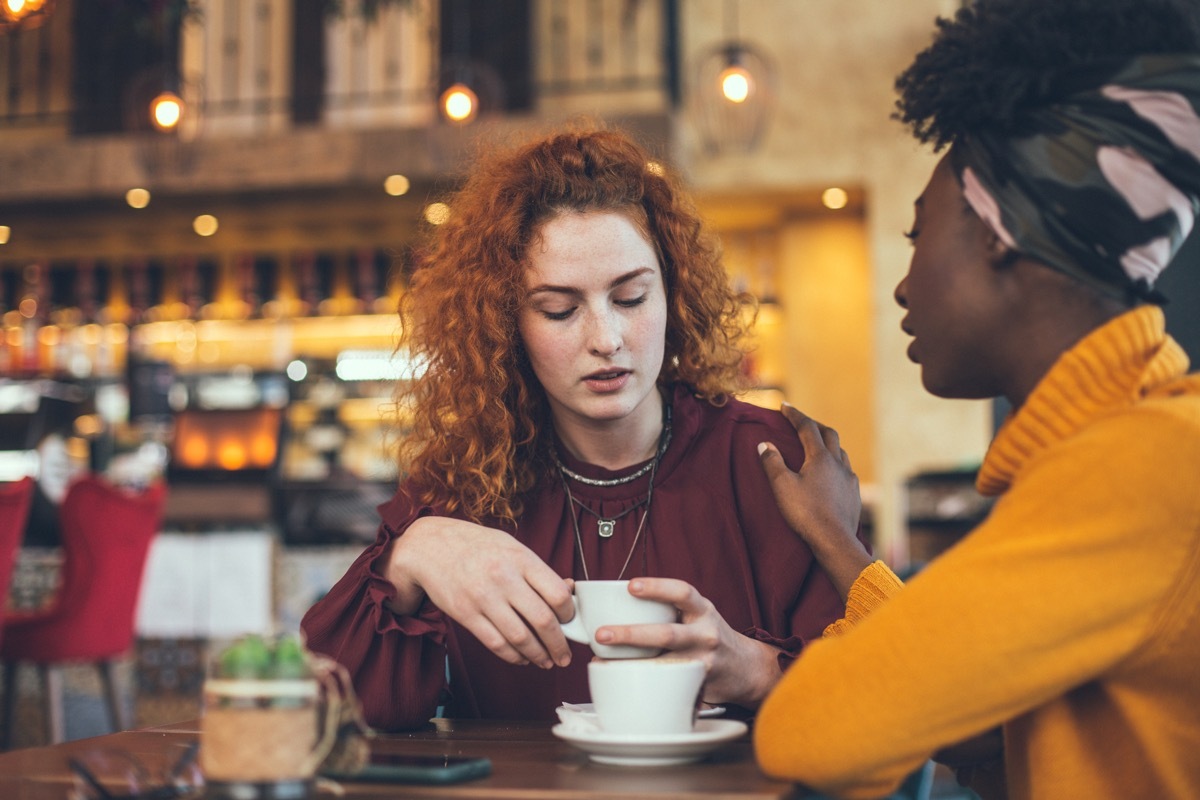 two female friends talking in a cafe, while one comforts the other