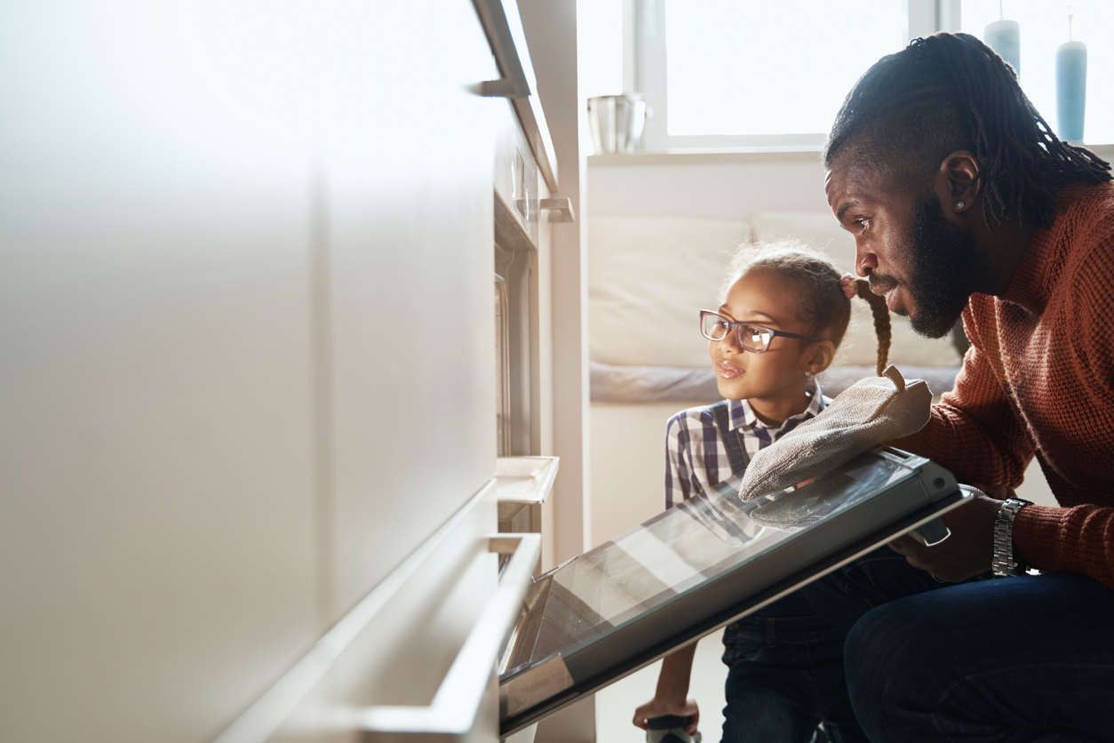 A young girl and a man looking into an oven while baking something