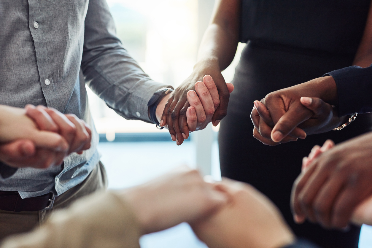 A cropped photo of a multiethnic group of worshipers join hands in a prayer circle