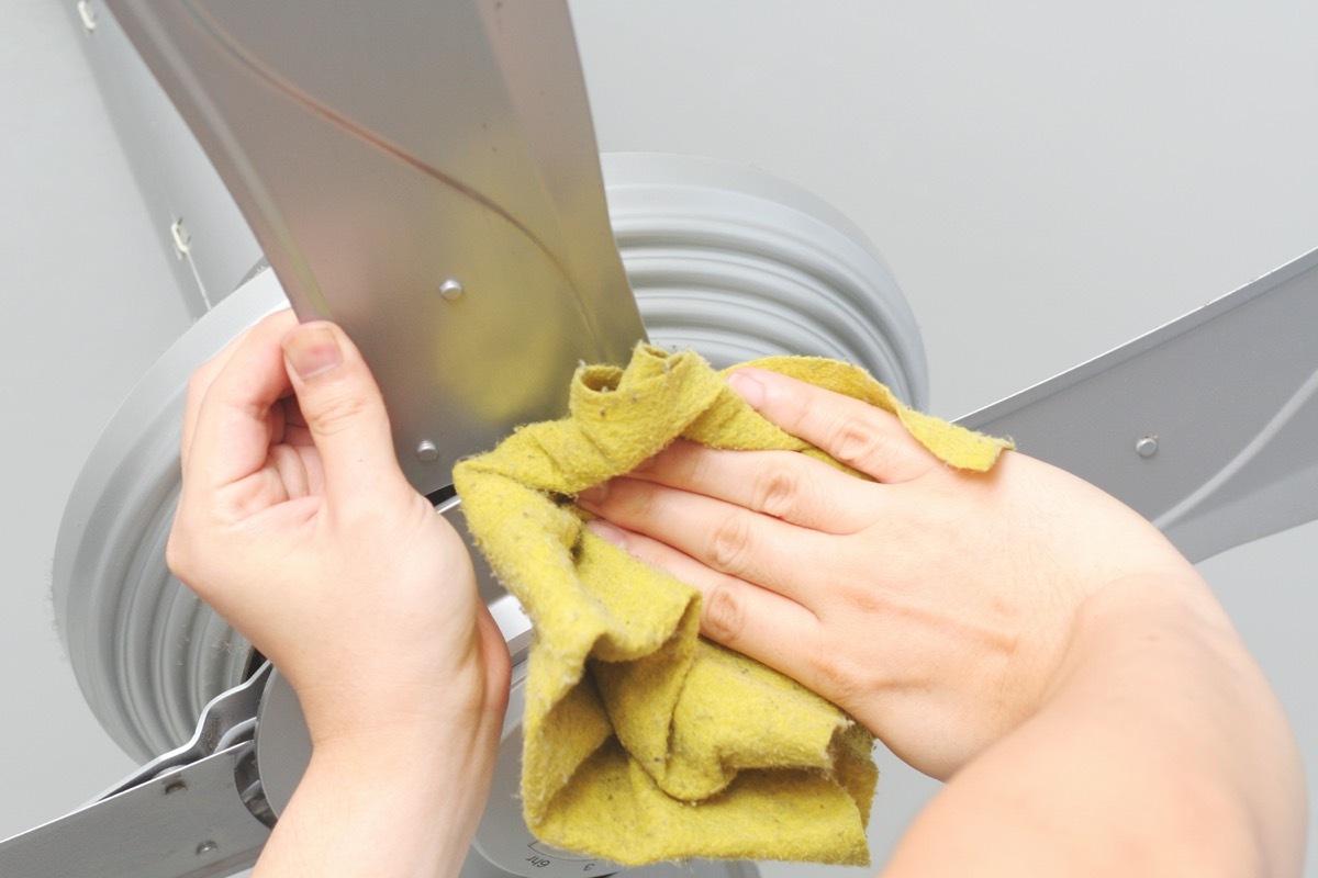 Cleaning the ceiling fan with a cloth.