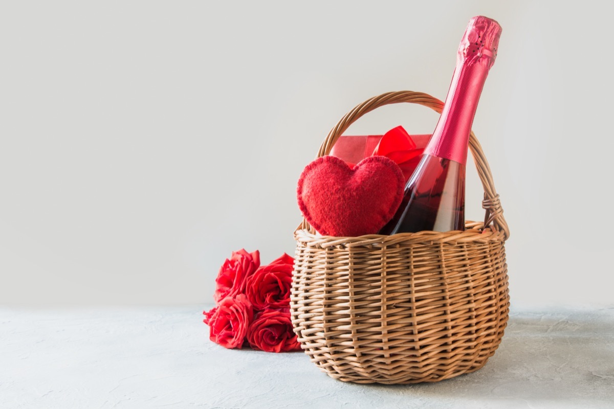 a bottle of champagne and red hart in a basket next to a bouquet of flowers