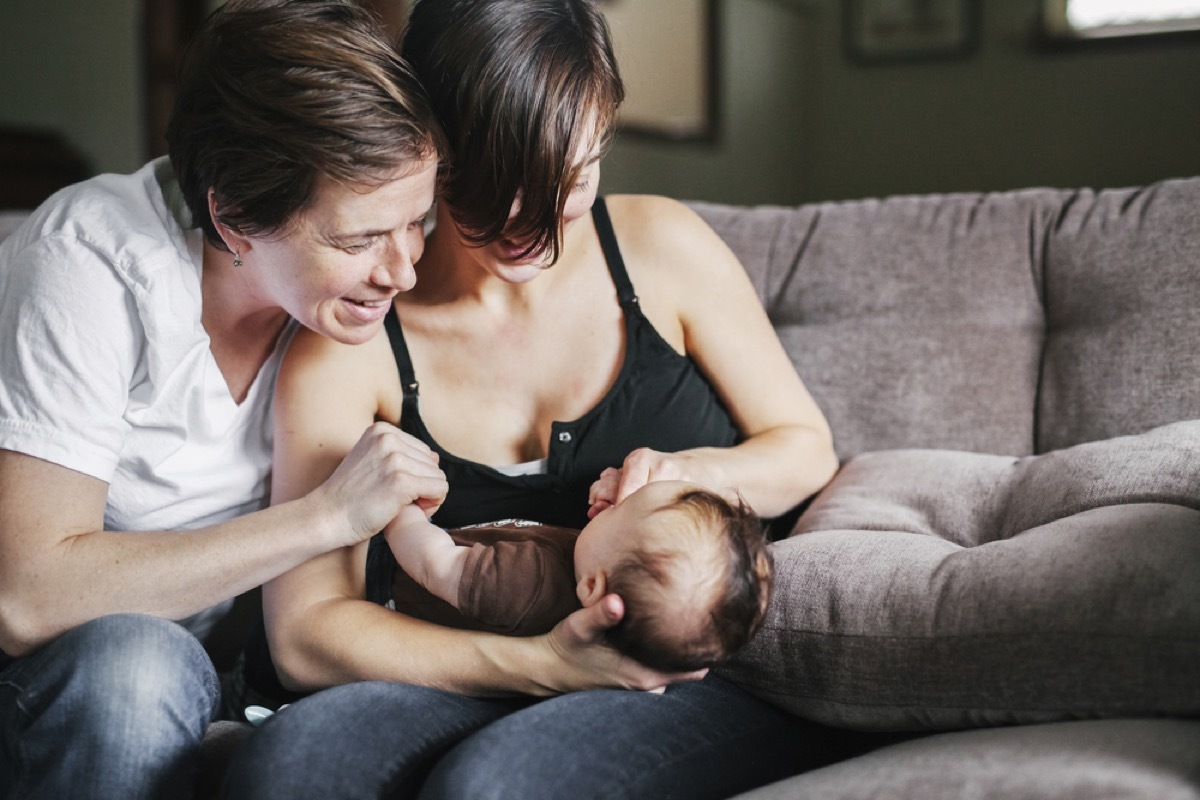 two moms holding young baby on gray couch