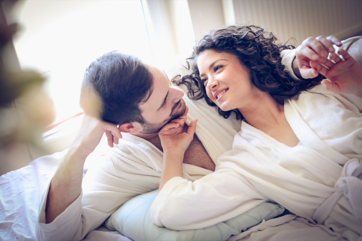 woman in robe touching a man's face in bed