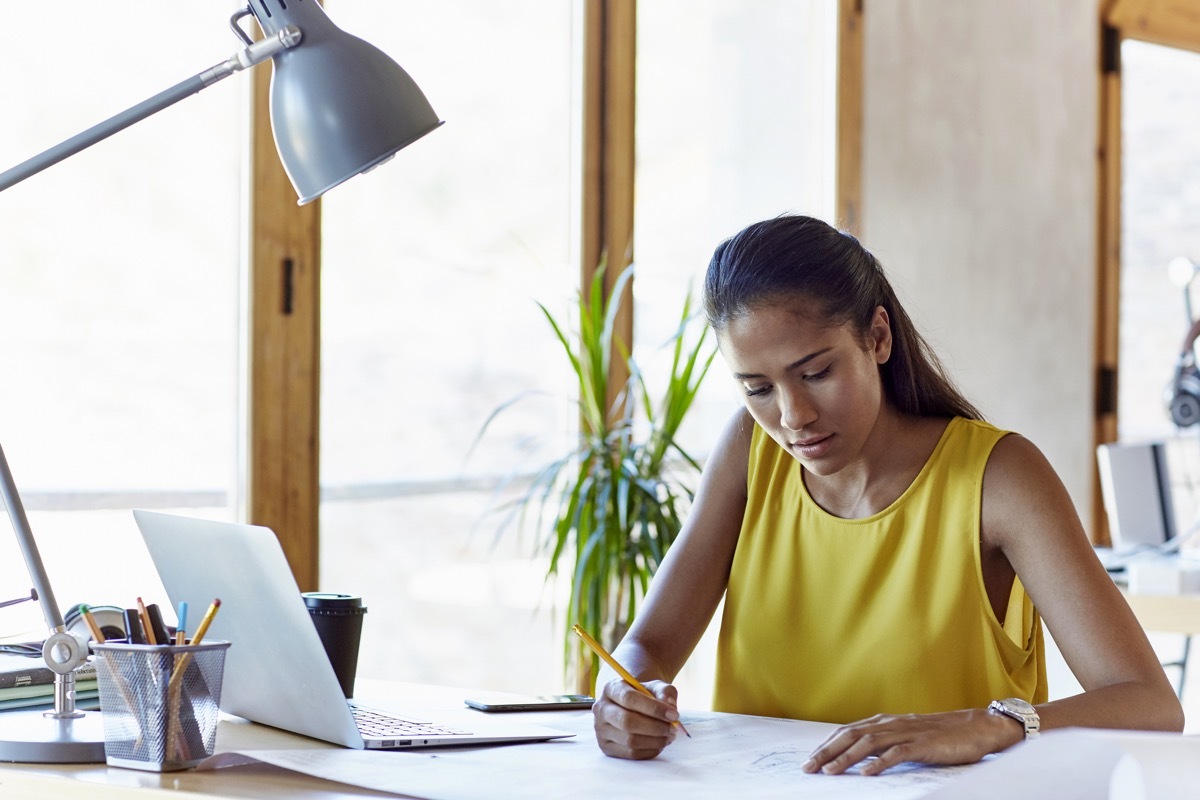 Young businesswoman analyzing blueprint at desk in creative office