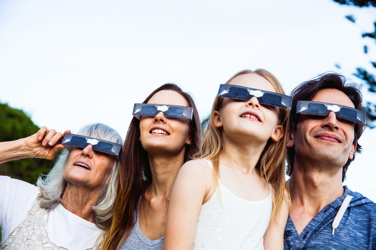 Family looking at Solar Eclipse using solar glasses. Parents with young daughter and grandmother.