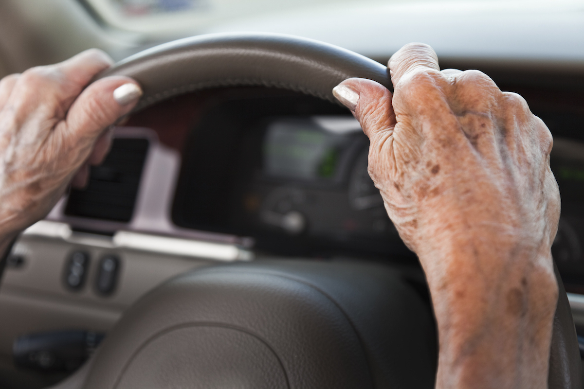 Senior woman driving car with hands on steering wheel.