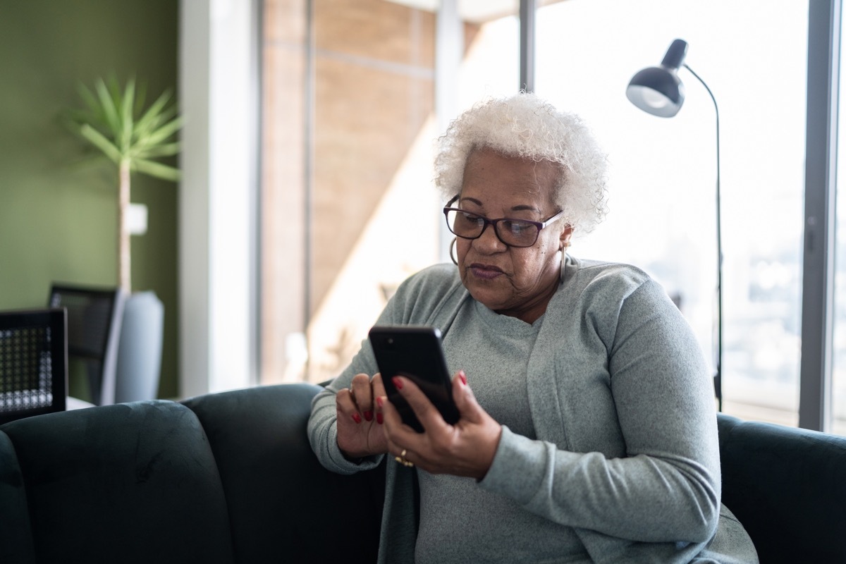 Senior woman using smartphone sitting on the couch at home