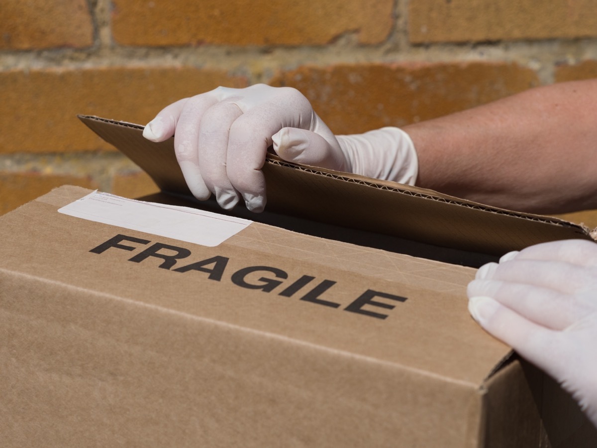 white person in latex gloves opening cardboard box