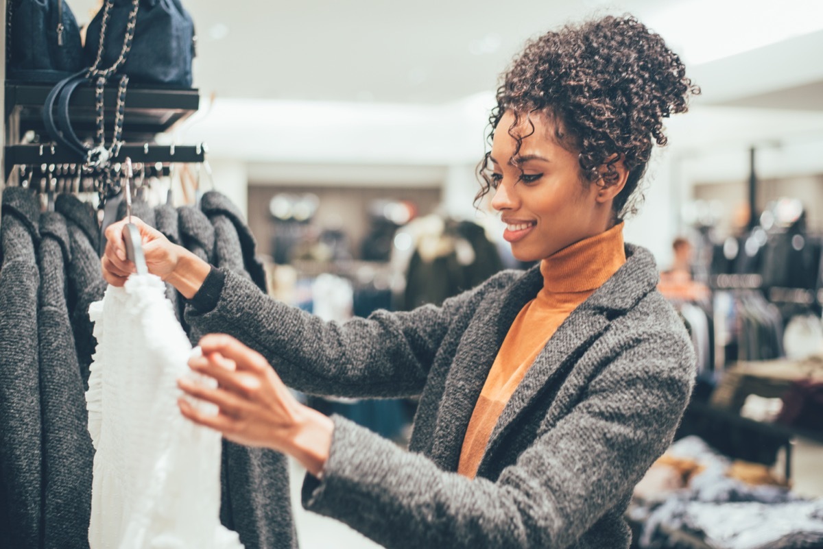 woman with curly hair in orange turtleneck and gray sweater clothing shopping