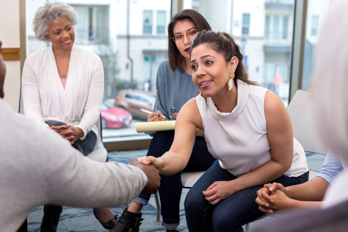 businesswoman sits with colleagues and reaches forward to shake hands with an unseen new client