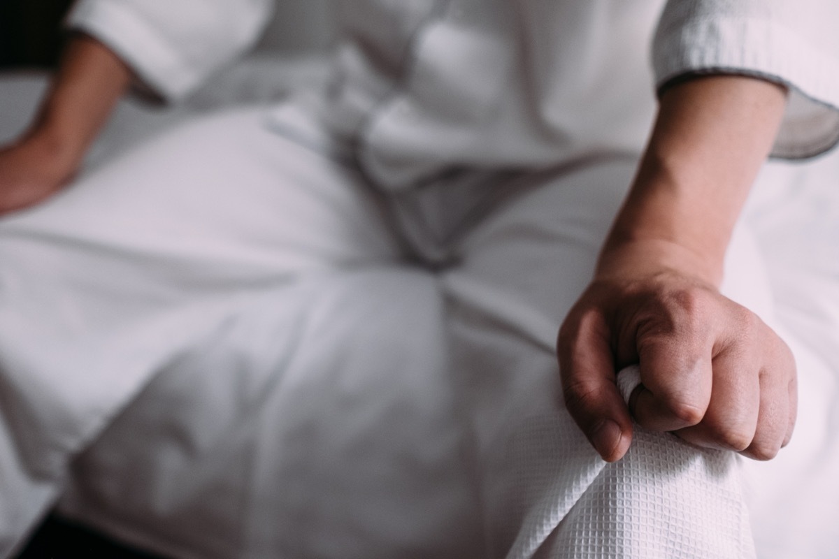 Image of a man sitting on the bed and putting his hands on his knees