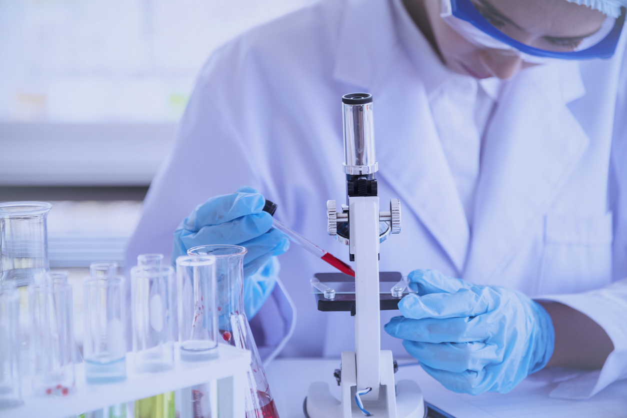 Medical researcher uses a dropper to place a red sample onto a microscope slide