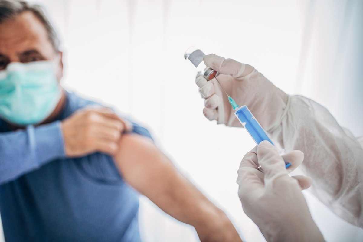 Two people, medical doctor in protective suit giving a senior male Covid-19 coronavirus vaccine.