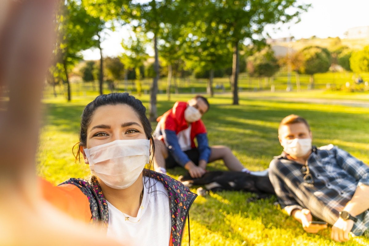 Cheerful university student taking selfie with friends sitting on grass.