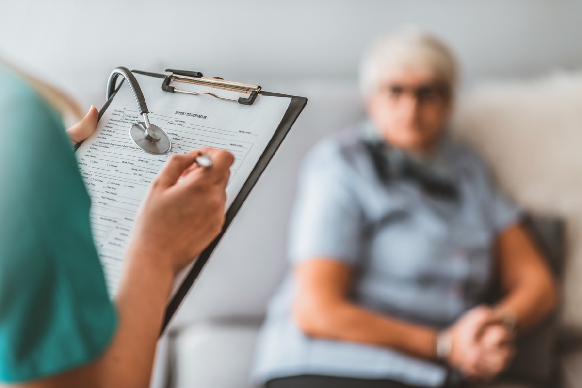 nurse writing on notepad while senior sits on couch