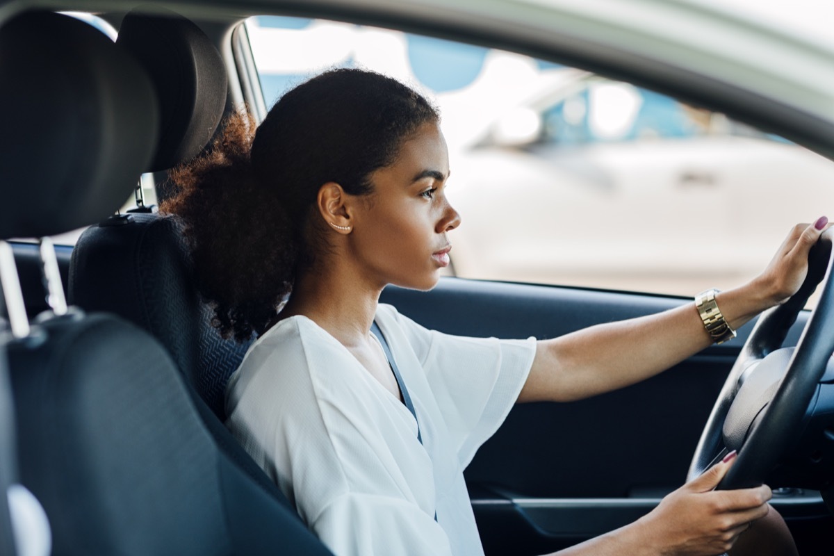 Side view of a woman sitting in a car holding a steering wheel and looking on the road