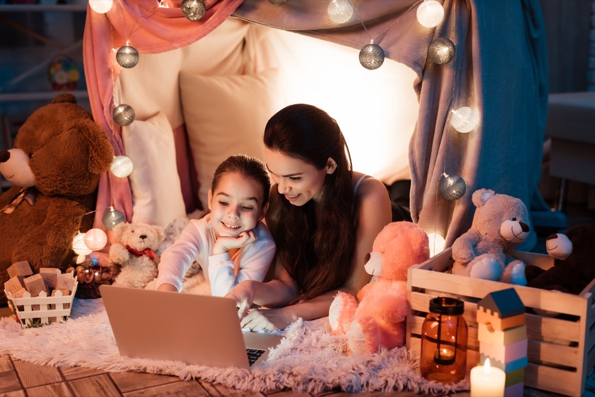 white mom and daughter watching movie in a pillow fort tent