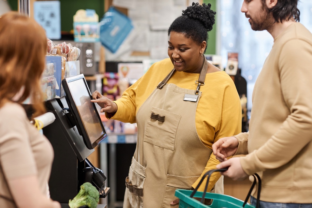 Waist up portrait of smiling woman helping customers with self checkout in supermarket