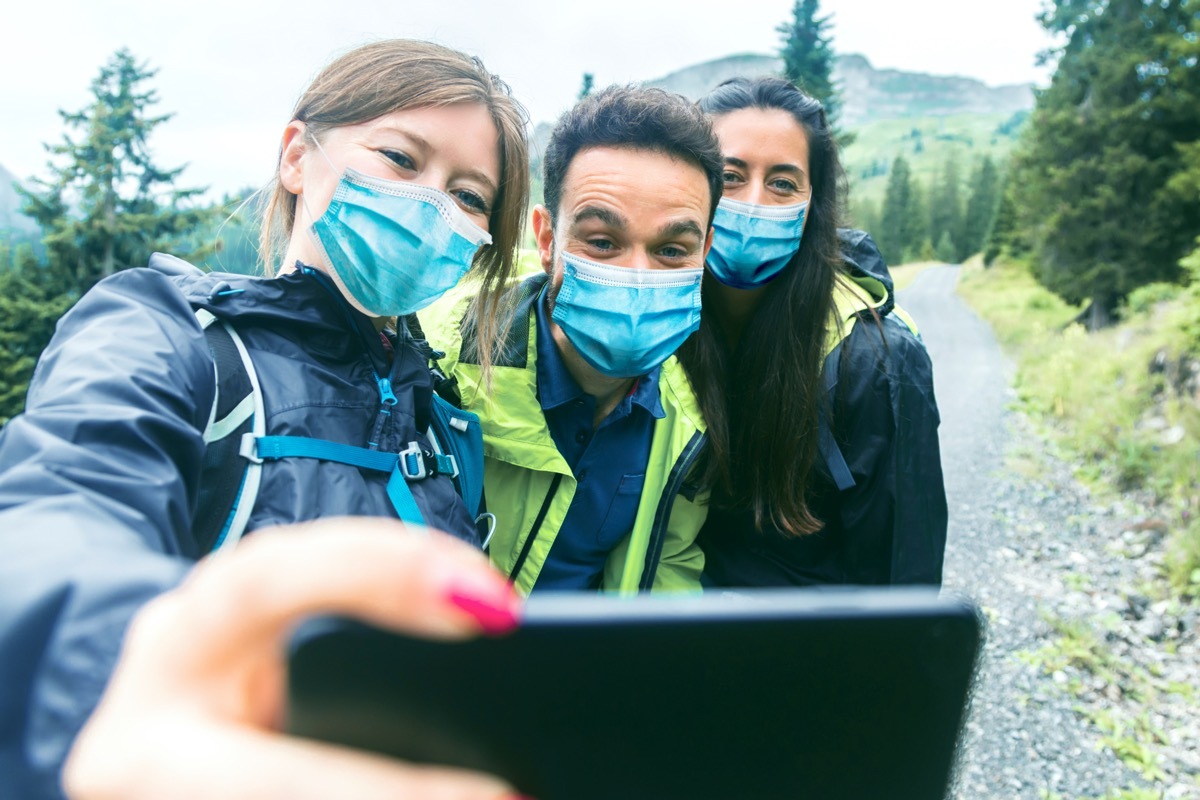 three friends take a selfie with masks on during a hike