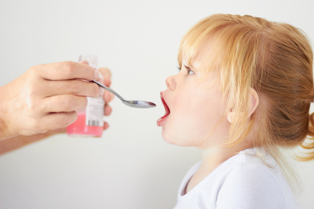 Little girl being given pink medicine.