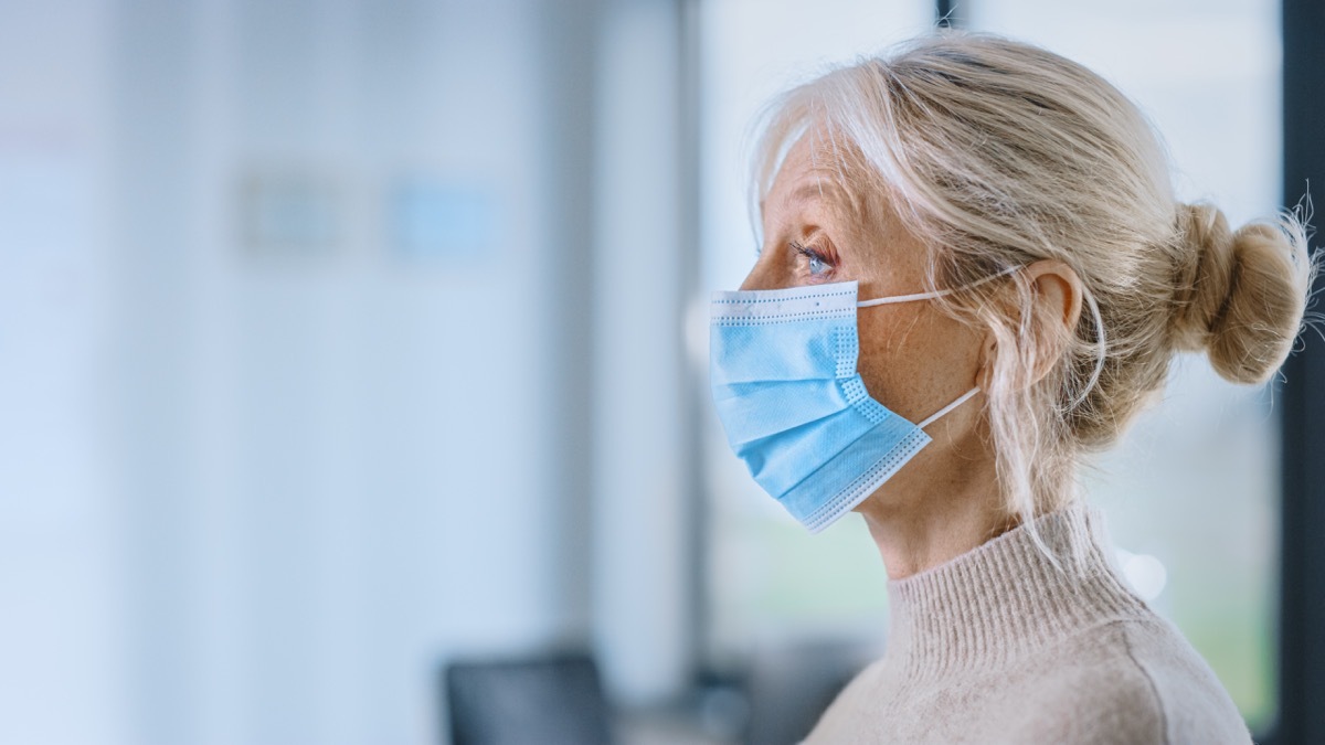 Close Up of a Senior Female Patient in Safety Protective Mask Ready for Measuring Body Temperature with Infrared Thermometer in a Health Clinic. Doctor Uses Touch-free Technology to Diagnose Symptoms.