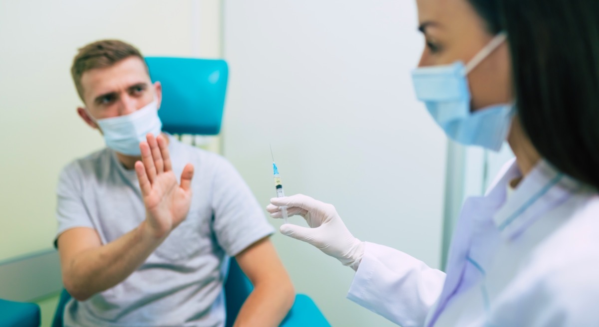 Man gesturing stop to nurse offering syringe with vaccine.