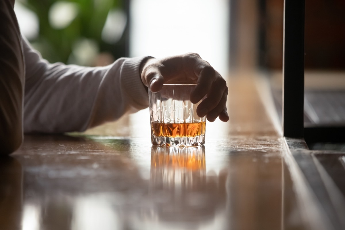 Man's hand holds whiskey glass at bar, 40 year old virgin