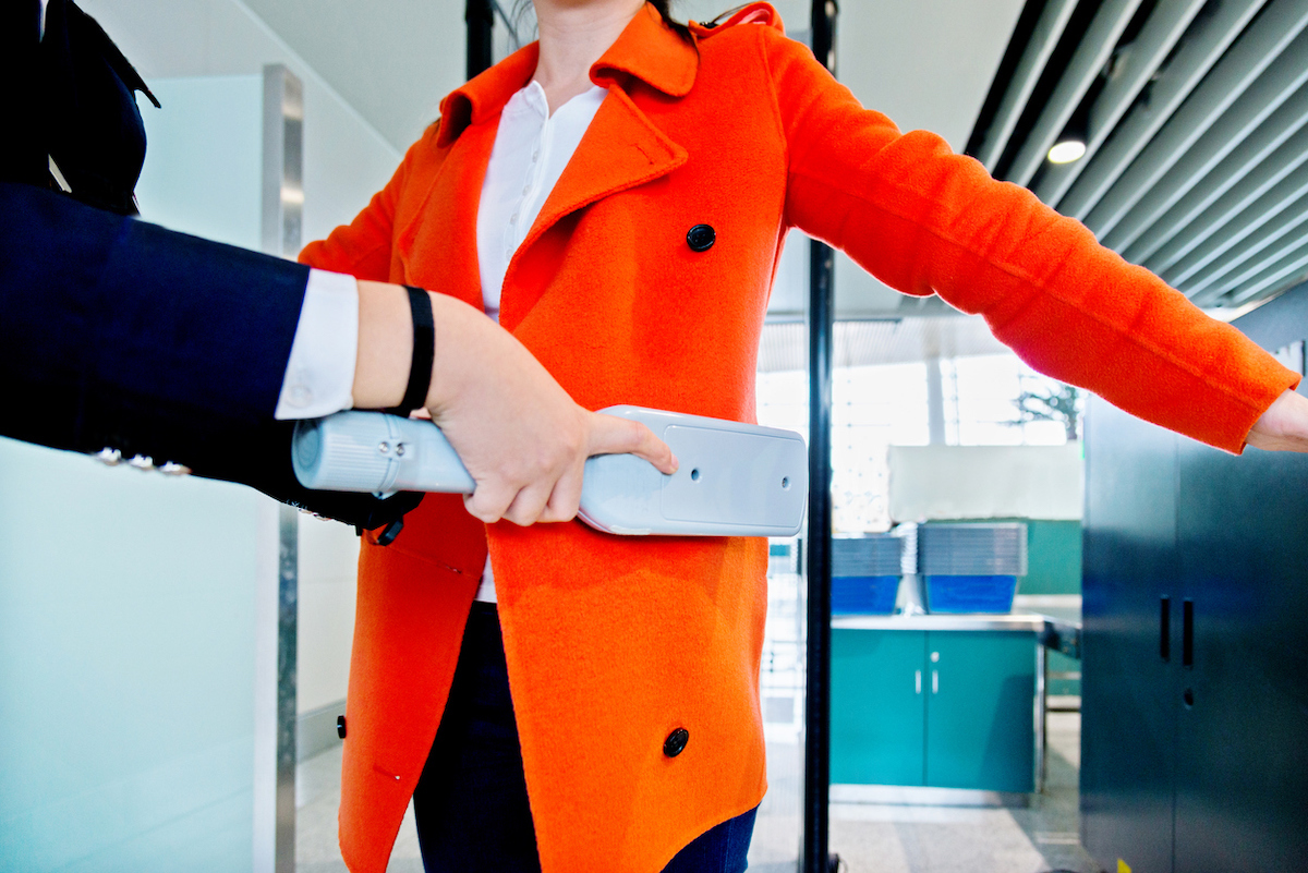 Close up of a woman in a bright orange coat being scanned with the metal detector at airport security.