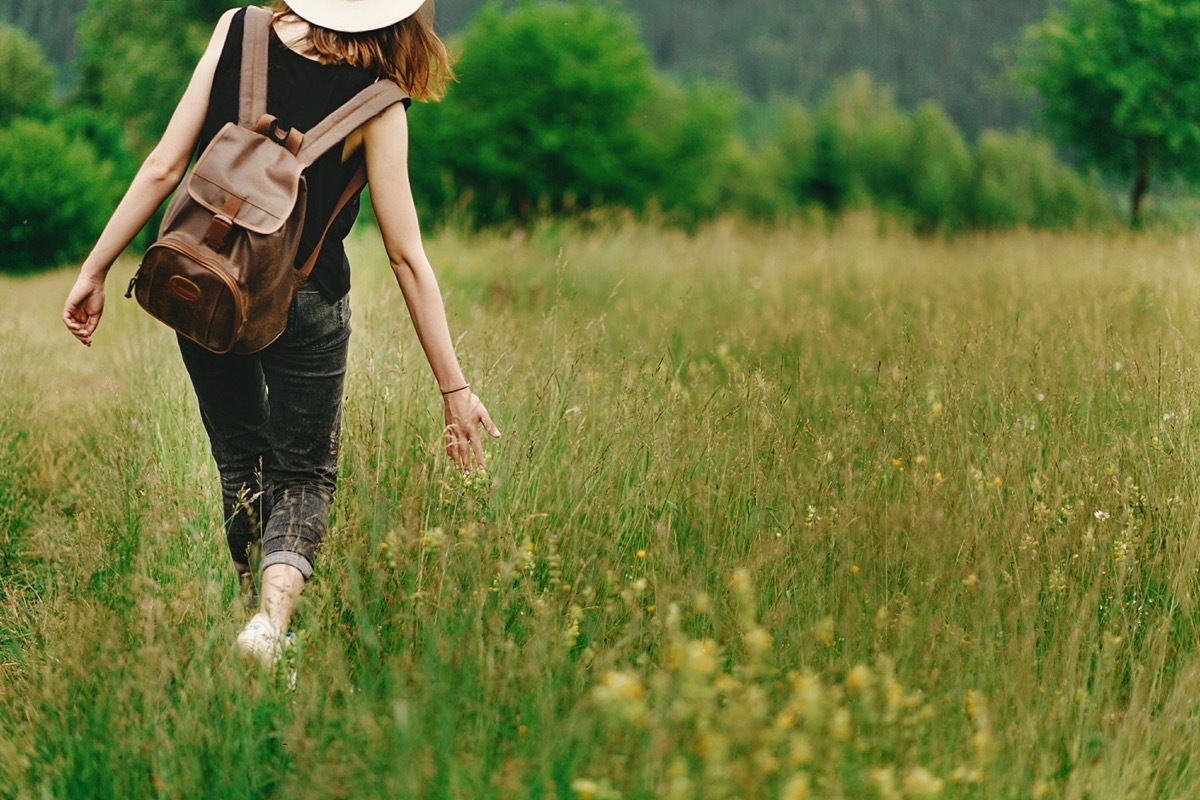 woman walking in grass and holding in hand herb wildflowers