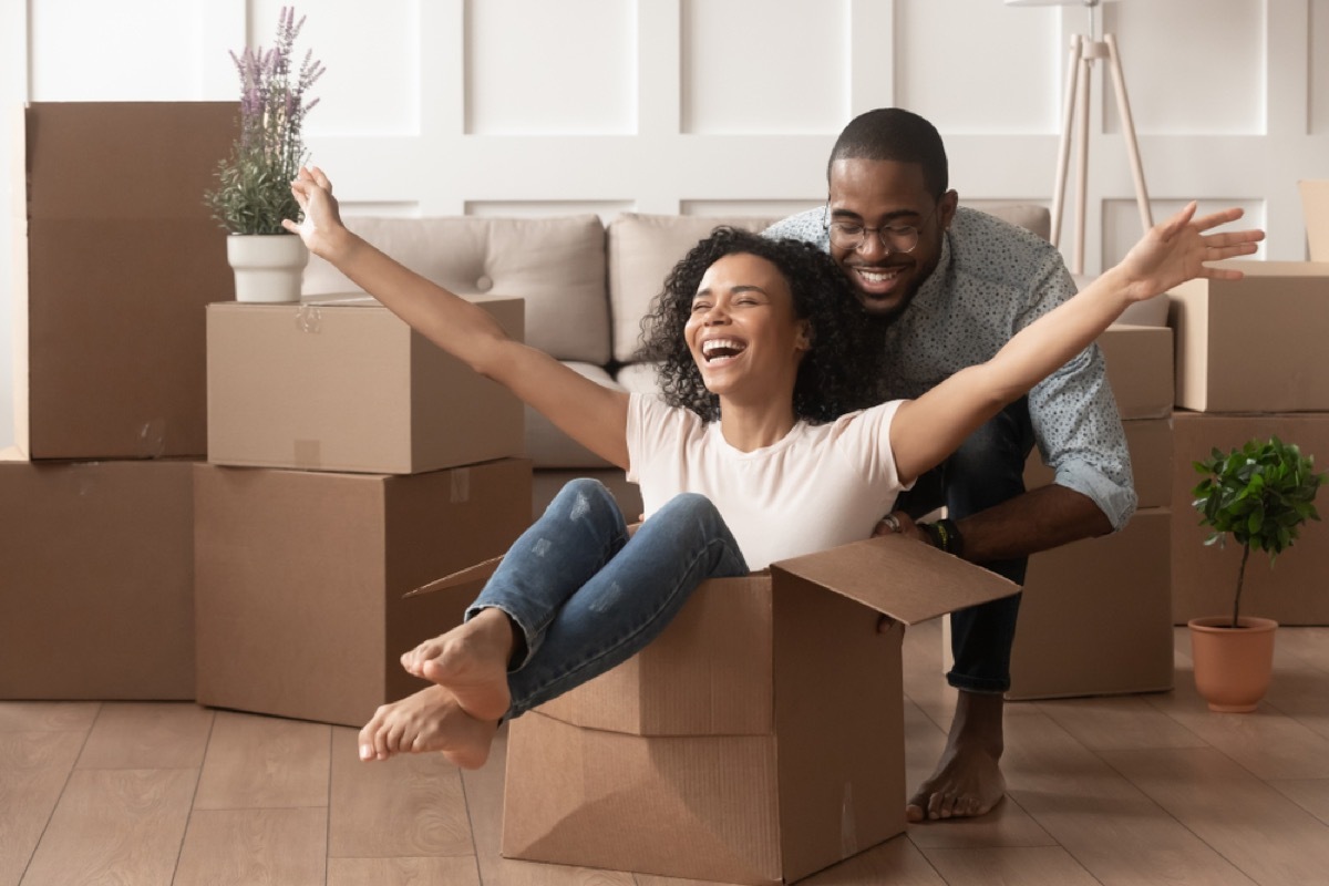 happy black woman sitting in a box with her husband behind her and other boxes