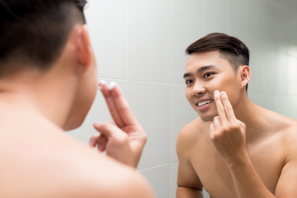 Young Asian man applying facial lotion in front of the mirror