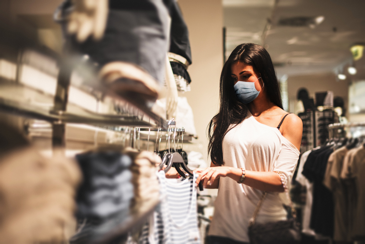 A young woman wearing a face mask shopping in a retail clothing store amid the coronavirus pandemic