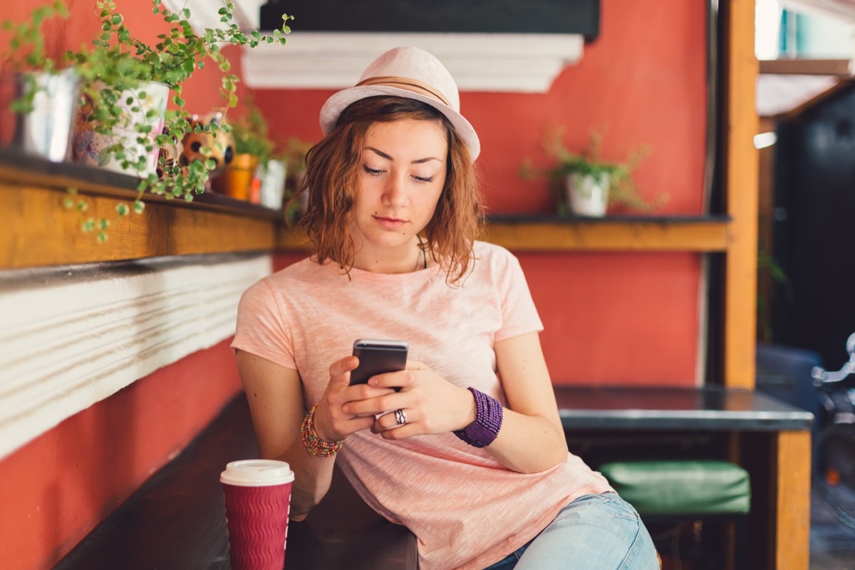 college student drinking coffee at cafe and using phone