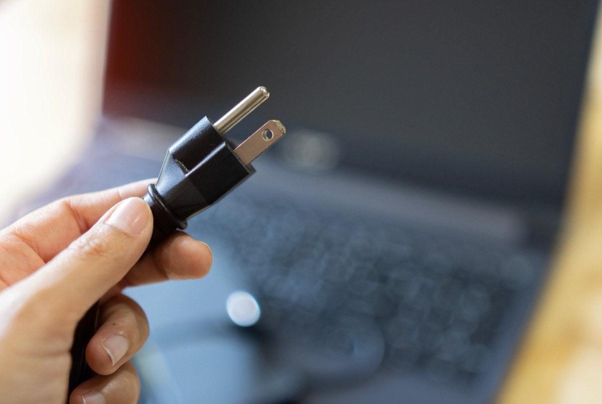 Selective focus. Women's hands are Plug in power outlet adapter cord charger of laptop computer.