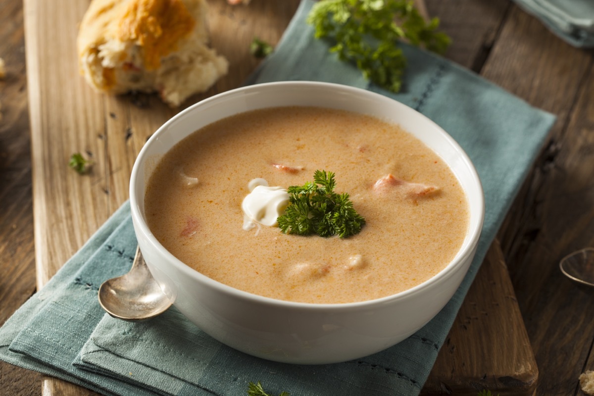 lobster bisque in white bowl on blue or green napkin on wooden table with bread in background